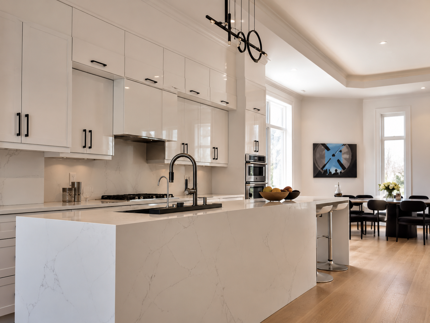 Modern white kitchen with custom cabinetry, marble island, recessed ceiling lights, pendant lighting, and a clean open dining area, representing professional electrical and renovation services in Toronto.